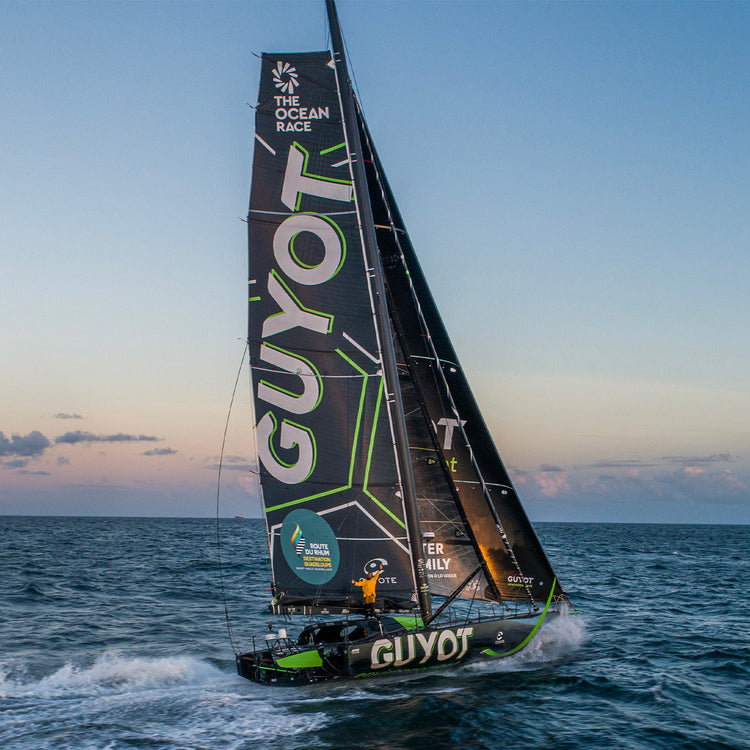 Square image of Team Guyot's green and black boat out on the ocean during a beautiful sunset in the background.//© Team Guyot | Charles Drapeau - ILP Vision