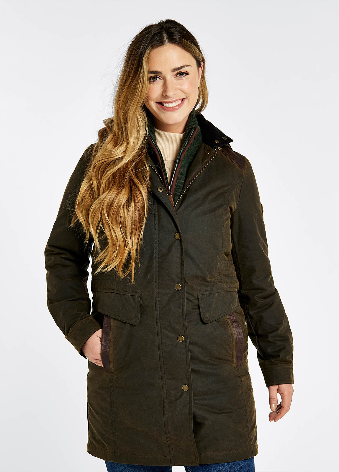 Waist up view of a female model wearing a Dubarry Blacklion Waxed cotton jacket, olive brown colour mid length coat with zip, buttons and mutiple pockets